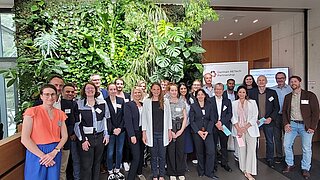 Gruppenfoto mit 24 Personen vor Pflanzenwand