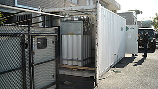 Blick in die HyTrA-Anlage mit Flaschen zur Wasserstoffspeicherung und ausgedienter Dieselgenerator links vorne