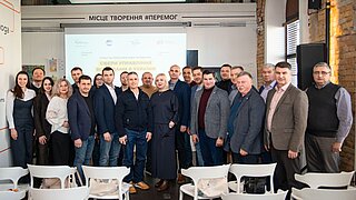 Eine Gruppe von vielen Personen steht in einem Konferenzraum.