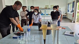 Personen stehen um einen Tisch, ein Mann mit Schutzbrille bediente ein Gerät