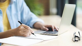 Person an Laptop, die sich etwas notiert